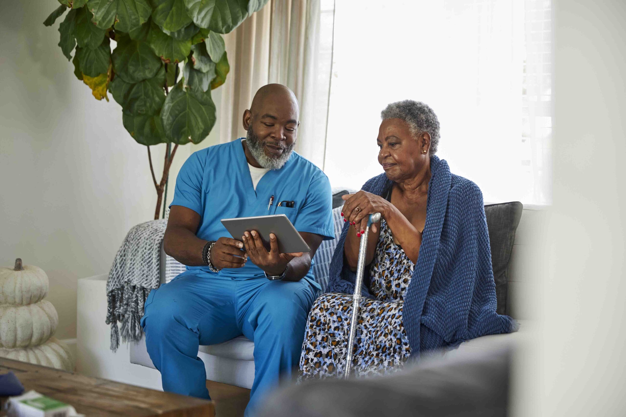 Mature male caregiver and senior woman looking at digital tablet at home